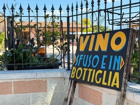 Een Italiaans bord bij een hek: vino sfuso e in bottiglia.