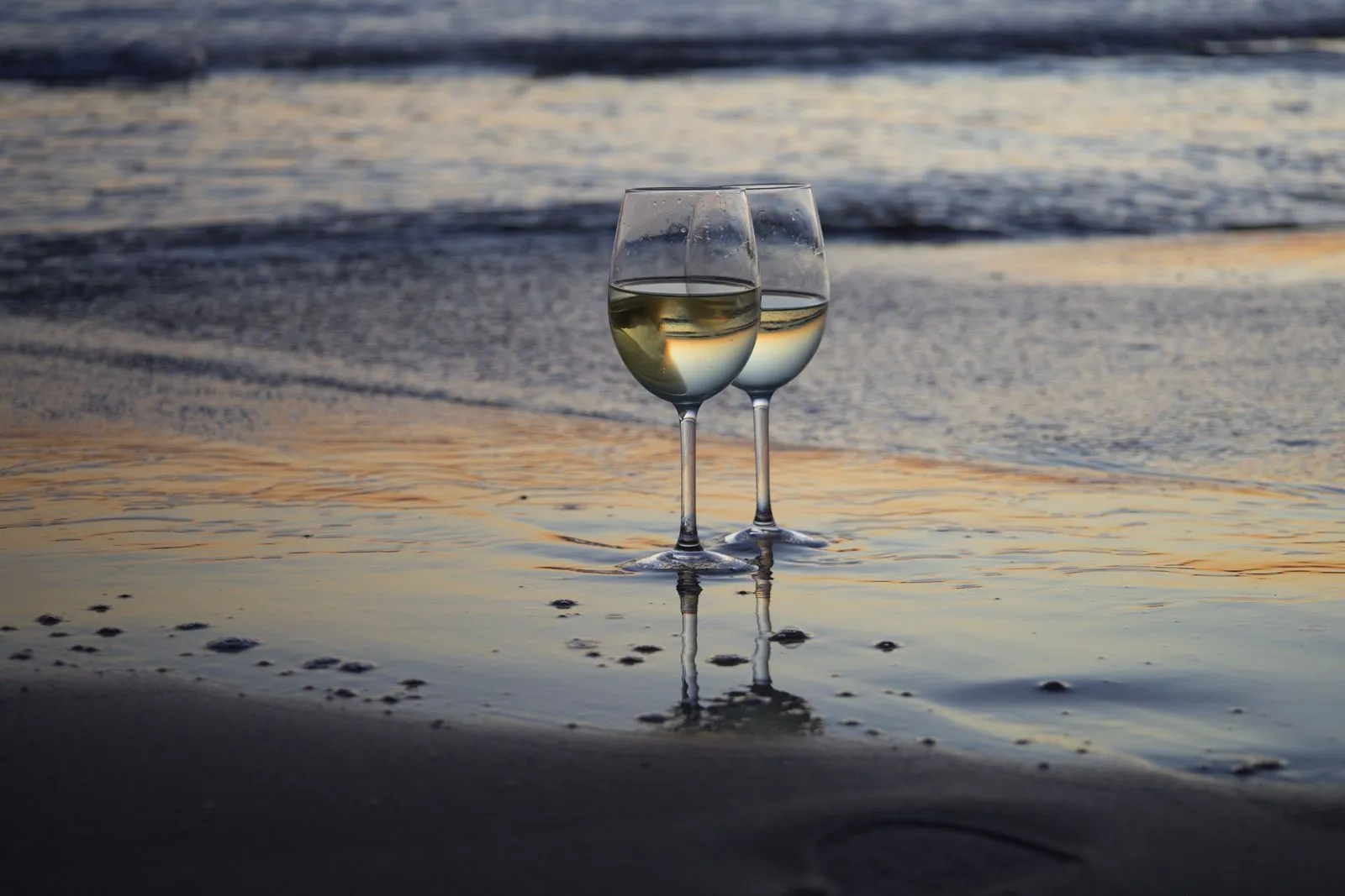 Glas witte wijn op het strand bij zacht avondlicht